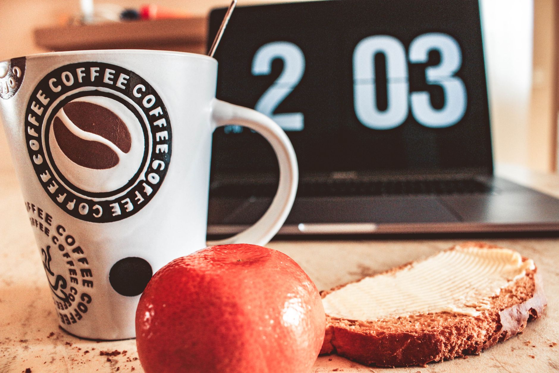 A cozy breakfast setup with coffee, bread and fruit next to a laptop.